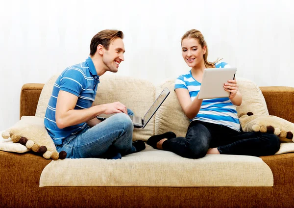 Casal jovem relaxante no sofá e usando tablet e laptop — Fotografia de Stock