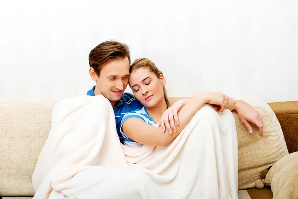 Usmívající se milující pár sedí na gauči s dekou — Stock fotografie