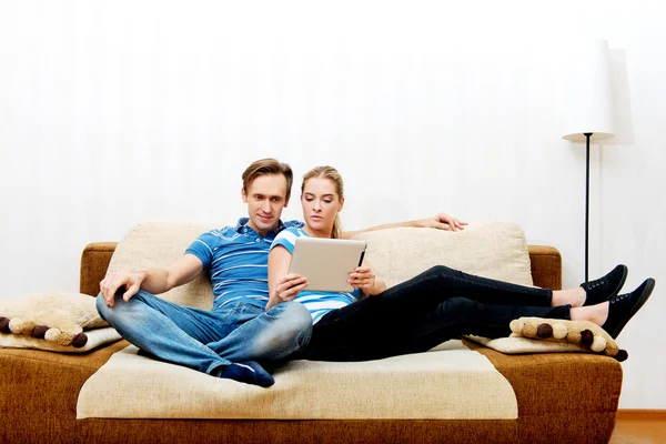 Casal jovem sentado em casa e à procura de algo no tablet — Fotografia de Stock