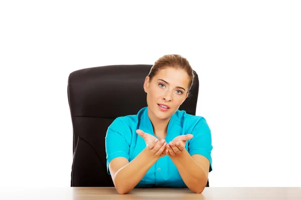 Junge Ärztin oder Krankenschwester, die hinter dem Schreibtisch sitzt und mit jemandem spricht — Stockfoto