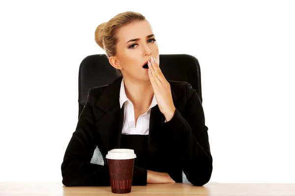 Yawning businesswoman drinking coffee from paper cup behind the desk — Stock Photo, Image