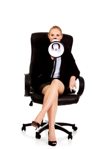 Business woman sitting on armchair and screaming through a megaphone — Stock Photo, Image