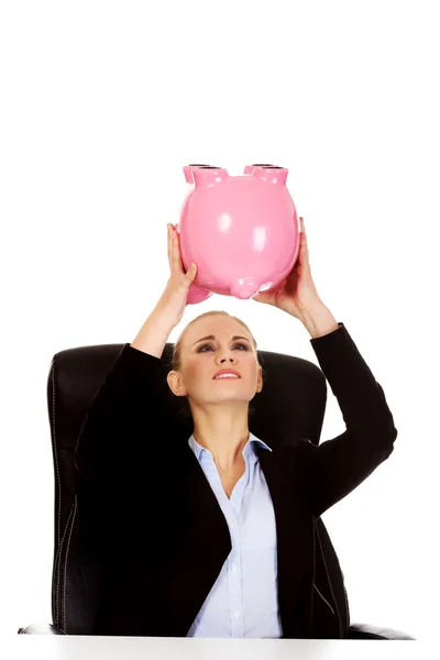 Worried business woman with a piggybank behind the desk — Stock Photo, Image