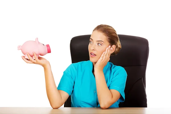 Young female doctor or nurse holding piggybank — Stock Photo, Image