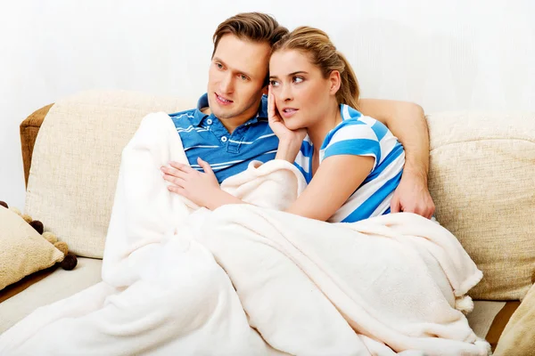 Sonriente pareja amorosa sentada en el sofá con manta — Foto de Stock