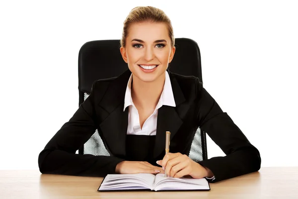 Sonriente mujer de negocios escribiendo nota junto a un escritorio — Foto de Stock