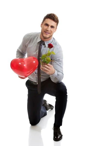 Hombre arrodillado con rosa roja y globo del corazón . — Foto de Stock