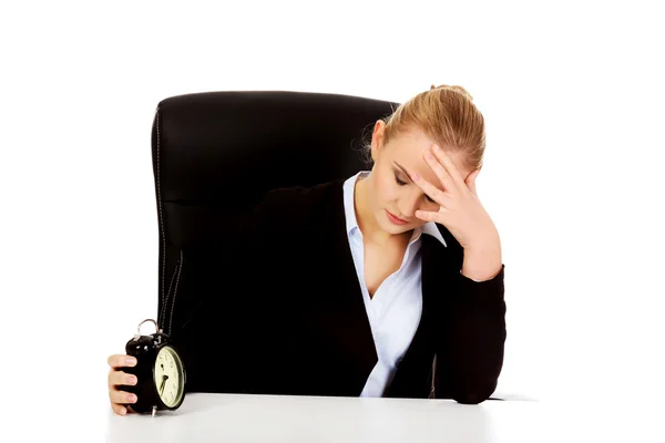 Tired business woman behind the desk with alarm clock — Stock Photo, Image