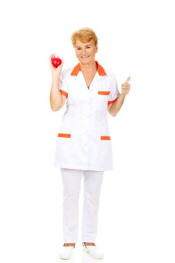 Yaşlı kadın doktor veya hemşire kırmızı oyuncak kalp tutan gülümse