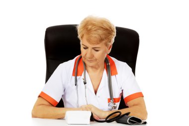 Yaşlı kadın doktor veya hemşire oturma bloog basınç ölçer ile masanın arkasında gülümse