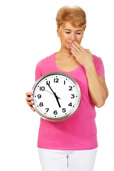 Zmęczony starszy kobieta trzyma zegar i ziewanie — Zdjęcie stockowe