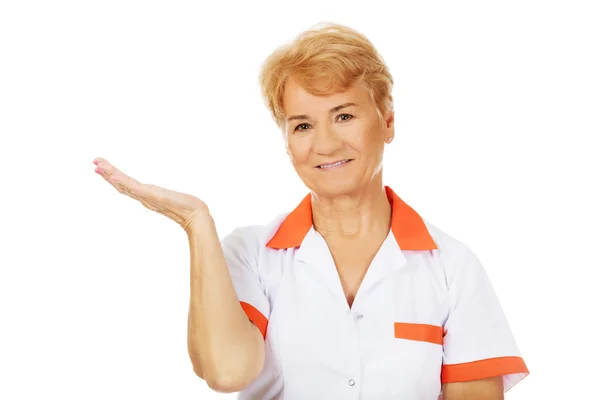 Glimlach van oudere vrouwelijke arts of verpleegkundige preseting iets op open palm — Stockfoto