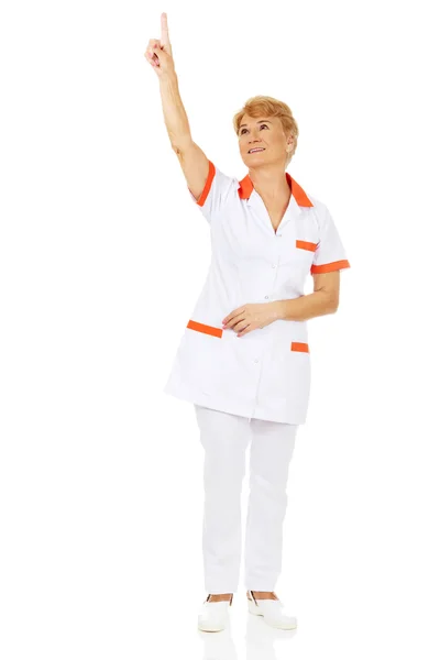 Smile elderly female doctor or nurse pointing up — Stock Photo, Image