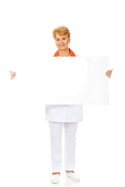 Leende äldre kvinnliga läkare eller sjuksköterska hålla tomt banner — Stockfoto