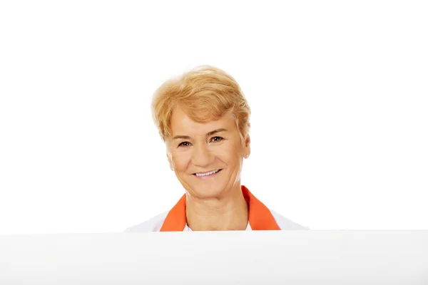 Yaşlı kadın doktor veya hemşire boş afiş tutarak gülümseyin — Stok fotoğraf