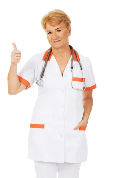 Улыбающаяся пожилая женщина-врач со стетоскопом показывает большой палец вверх — стоковое фото