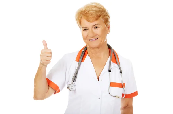 Sorriso anziano medico femminile con stetoscopio mostra pollice in su — Foto Stock