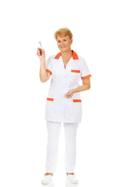 Sorria idosa médica ou enfermeira segurando tesoura — Fotografia de Stock
