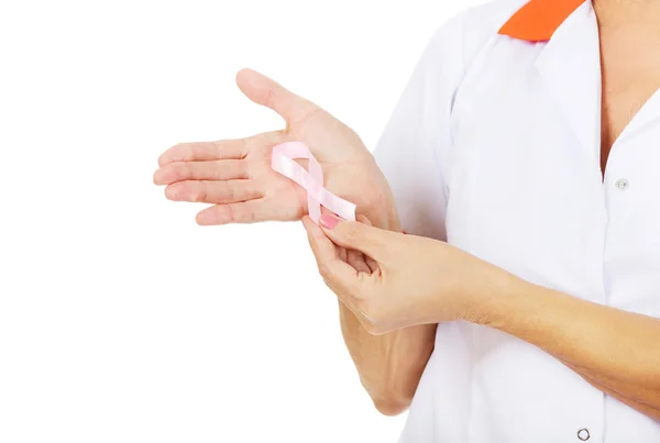 Elderly female doctor or nurse holds pink breast cancer awareness ribbon — Stock Photo, Image