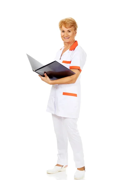 Elderly female doctor or nurse holds black binder and reads — Stock Photo, Image