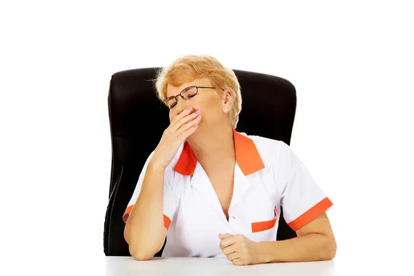 Yorgun yaşlı kadın doktor veya hemşire arkasında oturan Resepsiyon ve yawns — Stok fotoğraf
