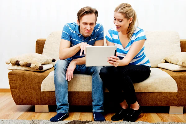 Casal jovem sentado em casa e à procura de algo no tablet — Fotografia de Stock