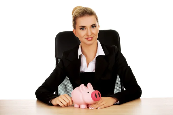 Geschäftsfrau mit Sparschwein hinter dem Schreibtisch — Stockfoto