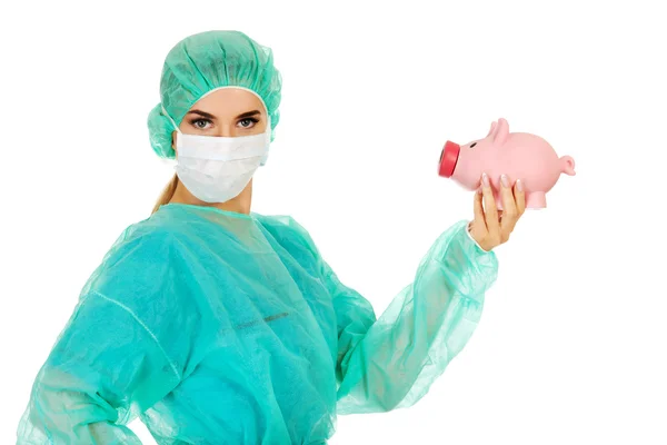 Female surgeon doctor holding piggy bank — Stock Photo, Image