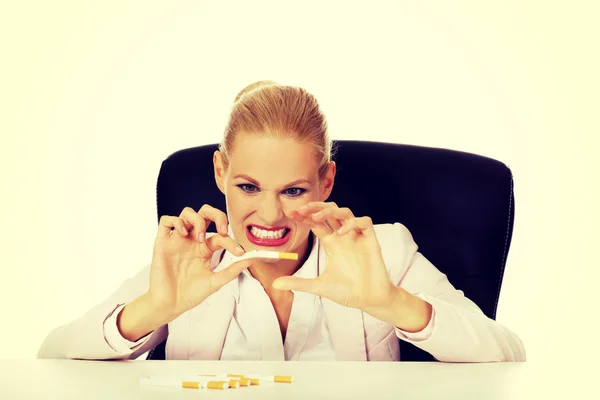 Angry business woman sitting behind the desk and breaking down cigarette — Stock Photo, Image