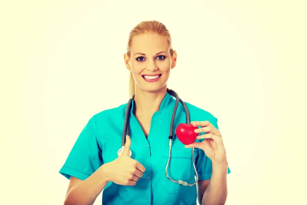 微笑的女医生听诊器持有心脏模型和拇指现身 — 图库照片