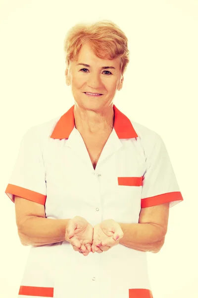 Sorridi anziana dottoressa o infermiera che presenta qualcosa a palme aperte — Foto Stock