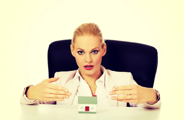 Geschäftsfrau sitzt hinter dem Schreibtisch mit Hausmodell — Stockfoto