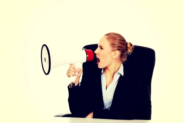 Mulher de negócios sentada atrás da mesa e gritando através de um megafone — Fotografia de Stock