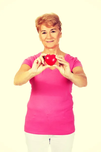 Vecchia donna sorridente che tiene il cuore rosso giocattolo — Foto Stock