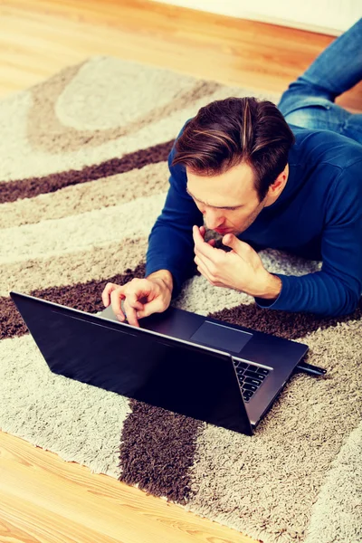 Młody człowiek leży na podłodze i używa laptopa — Zdjęcie stockowe