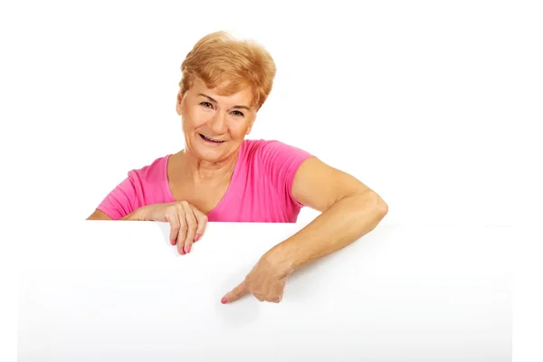 Oudere vrouw wijst naar iets op een leeg spandoek — Stockfoto