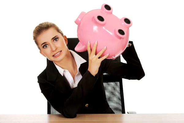 Besorgte Geschäftsfrau mit Sparschwein hinter dem Schreibtisch — Stockfoto