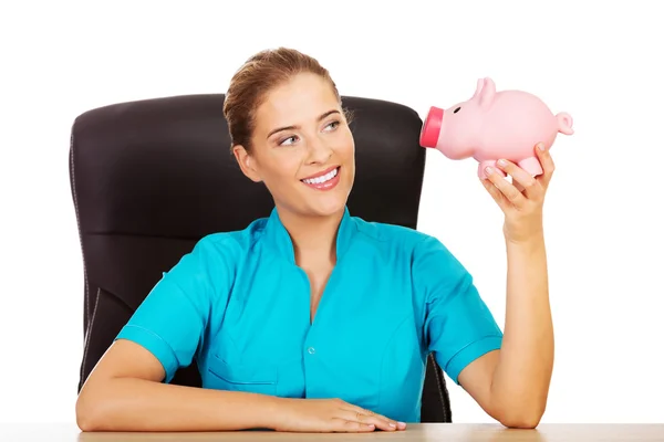 Young female doctor or nurse holding piggybank — Stock Photo, Image