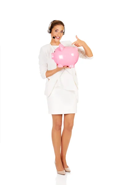 Young businesswoman in headset holding piggybank — Stock Photo, Image