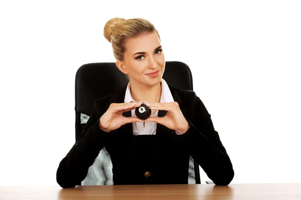 Businesswoman holding eight billiard ball by a desk — Stock Photo, Image