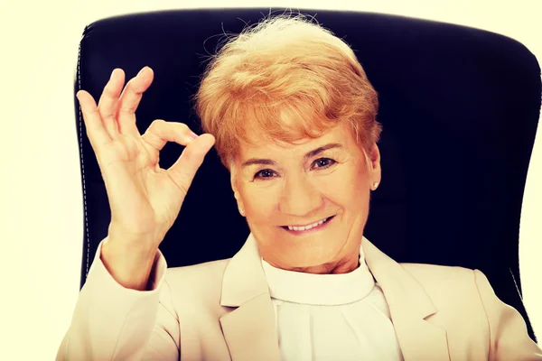 Smile elderly business woman sitting on armchair and show ok sign — Stock Photo, Image