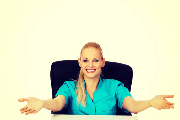 Lustige Ärztin oder Krankenschwester, die mit offenen Armen hinter dem Schreibtisch sitzt — Stockfoto