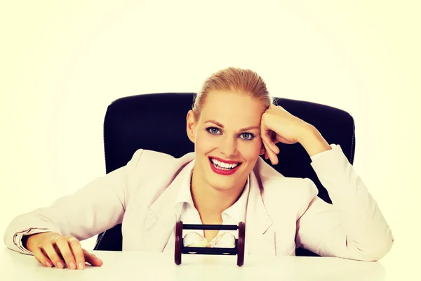 Happy business woman sitting behind the desk with sandglass — Stock Photo, Image