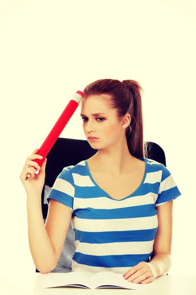 Teenager-Frau macht Hausaufgaben und hält riesigen Stift — Stockfoto