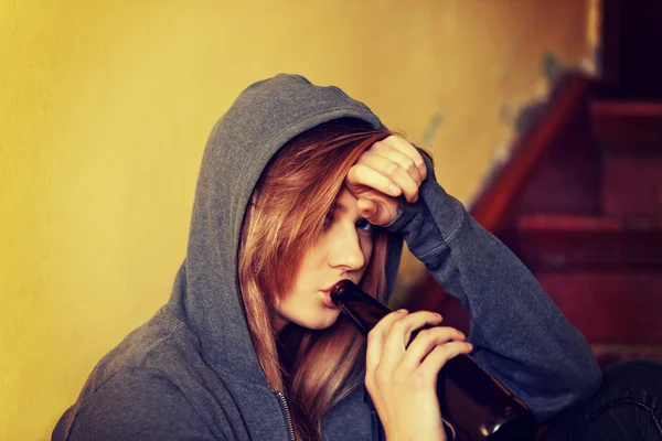 Teenage depressed woman sitting on the staircase and drinking a beer — Stock Photo, Image