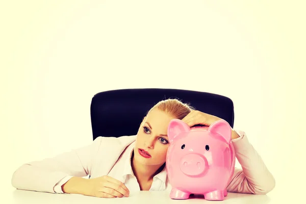 Worried business woman with a piggybank behind the desk — Stock Photo, Image