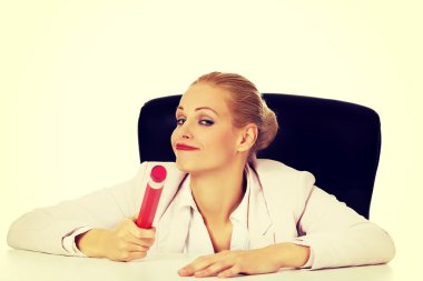 Genç iş kadını masanın arkasında oturuyor ve elinde büyük bir kalem tutuyor.