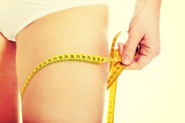 Sarı bantla kalçasını ölçen zayıf genç bir kadın.