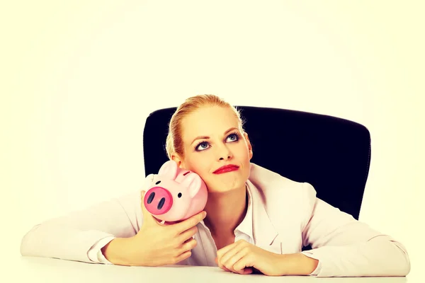 Mujer de negocios feliz con una hucha detrás del escritorio — Foto de Stock