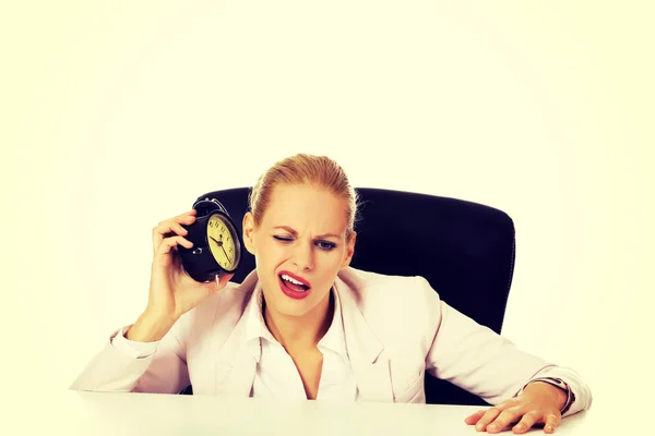 目覚まし時計にデスクと耳の後ろに座っている女性実業家 — ストック写真